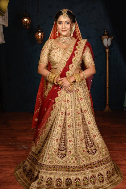 Stunning Indian bride dressed in traditional bridal lehenga with heavy gold jewellery and veil posing fashionable in studio lighting. Wedding fashion and lifestyle.